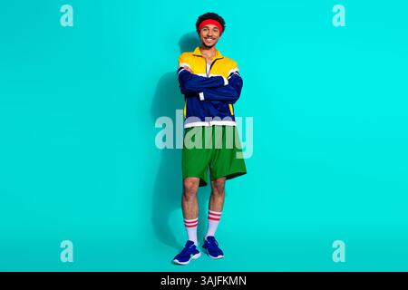 Homme sportif rétro dans des vêtements d'action colorés posant en toute confiance sur fond sarcelle Banque D'Images