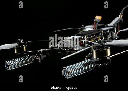 Vue rapprochée détaillée d'un drone de course compact avec ses hélices, ses moteurs, sa caméra et ses composants électroniques complexes sur fond sombre. Banque D'Images