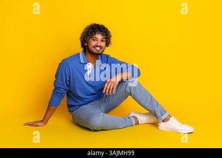 Jeune homme élégant dans un polo bleu posant sur un fond jaune vif, mettant en valeur la mode décontractée Banque D'Images