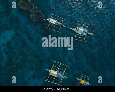 Vue aérienne des bateaux traditionnels philippins naviguant dans des eaux bleues cristallines, mettant en valeur la beauté tropicale et la culture maritime dynamique Banque D'Images