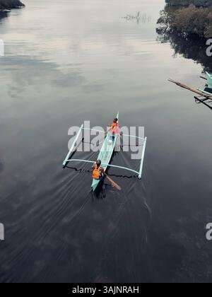 Vue aérienne d'un canot traditionnel philippin en saillie pagayé par deux personnes sur une eau tranquille, reflétant la beauté culturelle des Philippines Banque D'Images