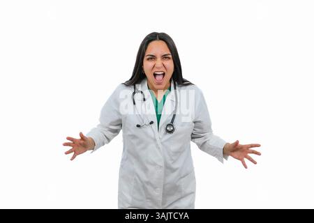 Jeune médecin féminin latin portant un manteau blanc et un stéthoscope criant avec les mains ouvertes et la bouche ouverte, exprimant la colère, la frustration ou la surprise sur un Banque D'Images