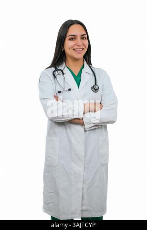 Vertical jeune femme latine médecin souriant portant stéthoscope et blouse de laboratoire croisant les bras, debout sur fond blanc, représentant les soins de santé, confi Banque D'Images