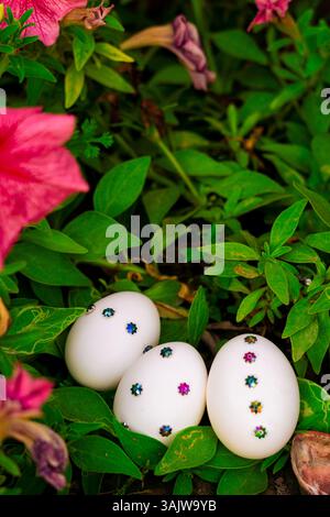Une charmante installation de Pâques avec des œufs blancs décorés nichés dans l'herbe verte, entourés d'éléments floraux, parfaits pour les cartes de vœux, les bannières et les holi Banque D'Images