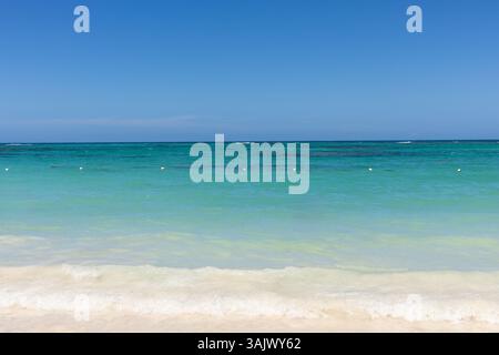 Les eaux turquoises vibrantes se baignent doucement contre une plage de sable blanc sous un ciel bleu vif, créant une atmosphère tranquille idéale pour la détente et le plaisir Banque D'Images