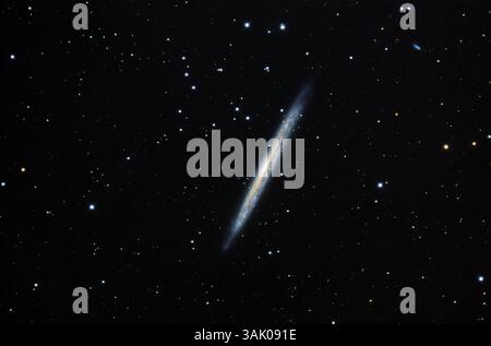 Galaxie splinter (NGC 5907), image optique. Située à environ 40 millions d'années-lumière de la Terre dans la constellation du Draco, NGC 5907 est une galaxie spirale, vue ici côte à côte. Le bord extérieur de la galaxie apparaît bleu en raison des étoiles chaudes nées dans les bras spiraux, tandis que le noyau jaune contient des étoiles plus anciennes et plus froides. Une ruelle de poussière sombre à travers la galaxie est juste visible comme une strie rougeâtre. Banque D'Images