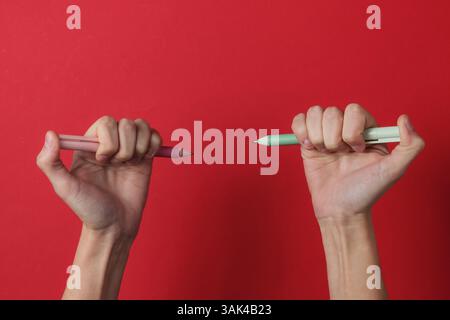 Ambidextr. Les mains féminines tiennent des stylos sur un fond rouge. Vue de dessus. Prise de vue en studio Banque D'Images