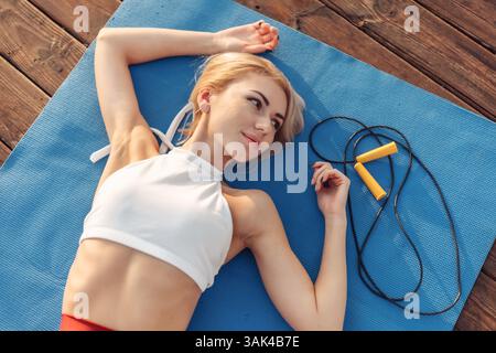 Femme de fitness de beauté dans les vêtements de sport se trouve sur mat en plein air. Concept de mode de vie sain Banque D'Images