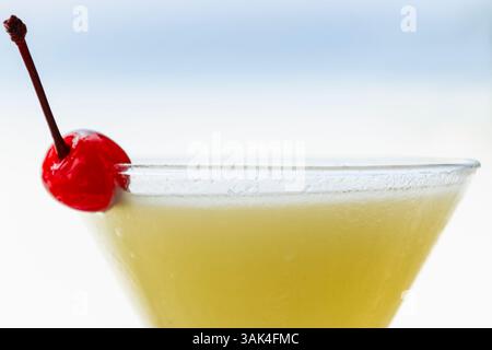 Ce gros plan invitant présente un cocktail Pina colada magnifiquement conçu, garni d'une cerise brillante, mettant en valeur sa teinte citronnée rafraîchissante. Banque D'Images