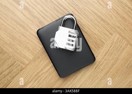 Disque dur externe et cadenas à combinaison sur table en bois clair, vue de dessus Banque D'Images