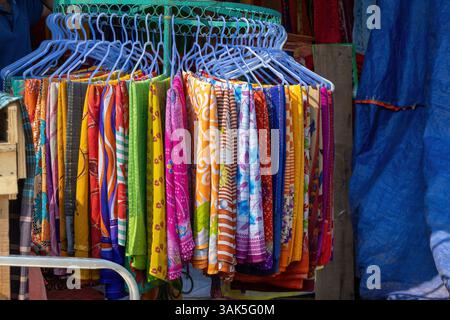 Sarees colorées en coton textile pour femmes, y compris des motifs imprimés et batik, accrochés sur des cintres à une façade de magasin pour la vente touristique à l'international Banque D'Images