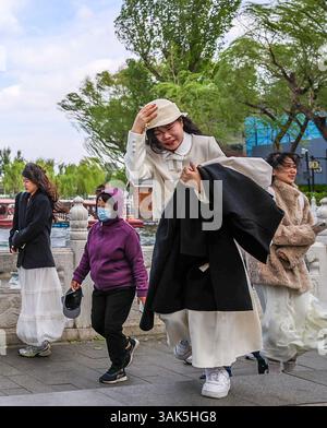 Pékin, Chine. 12 avril 2025. Les gens marchent dans la zone pittoresque de Shichahai à Pékin, capitale de la Chine, le 12 avril 2025. De nombreuses régions du nord de la Chine subissent des vents de force de vent et des baisses de température samedi. Crédit : Jiang Han/Xinhua/Alamy Live News Banque D'Images