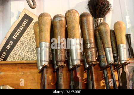 Jeu vintage d'outils à main avec poignées en bois et pointes en métal, à côté d'un tableau de conversion de mesure Banque D'Images