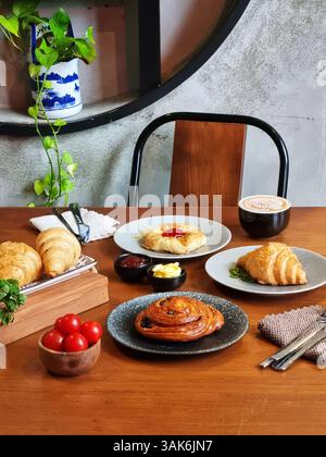 Plusieurs croissants fraîchement cuits sur une assiette en céramique, à côté d'une tasse de café, un petit pot de crème et de confiture. Cette image convient aux menus de café, foo Banque D'Images