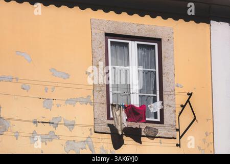 Une façade de bâtiment altérée à Bairro Alto, Lisbonne, dispose d'une fenêtre minimaliste avec du linge qui traîne à sécher, reflétant le Lif quotidien traditionnel Banque D'Images