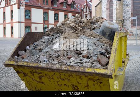Un conteneur en métal jaune rempli de débris de construction se dresse sur une place devant des bâtiments historiques Banque D'Images