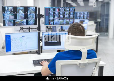 Agent de sécurité surveillant plusieurs écrans de surveillance dans une salle de contrôle high-tech pour la sécurité et la surveillance Banque D'Images