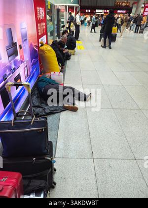 Pékin, Chine, 12 avril 2025 — les travailleurs migrants âgés reposent sur le sol à la gare ferroviaire sud de Pékin, au milieu de graves perturbations dues au vent, causant des retards et des annulations généralisés dans les services ferroviaires à grande vitesse dans le nord de la Chine. Banque D'Images