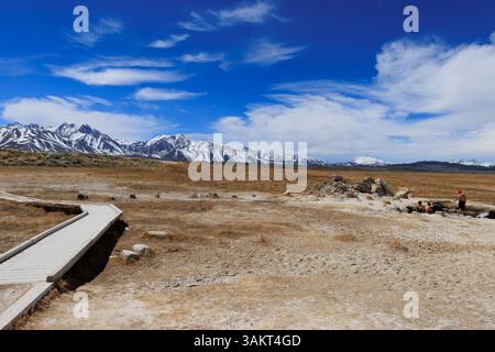 Mammoth Lakes, CA. 10 avril 2025. Une passerelle en bois s'étend devant les baigneurs baignant dans la source chaude de Wild Willie. Banque D'Images