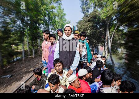 Les passagers montent sur le toit d'un train à vitesse excessive au Bangladesh, mettant en évidence les transports surpeuplés et les difficultés de voyage pendant les vacances chargées. Banque D'Images