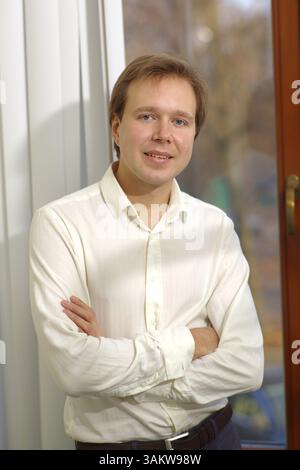 Heureux jeune homme en chemise blanche et bras croisés debout près de la fenêtre avec stores ouverts Banque D'Images