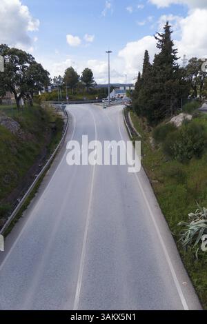 Vue panoramique d'une route vide à deux voies s'étendant vers un rond-point, encadrée par des arbres et sous un ciel nuageux Banque D'Images