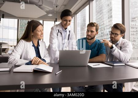 L'équipe enthousiaste de médecins polyethnic tient la conversation en regardant l'écran de l'ordinateur portable Banque D'Images