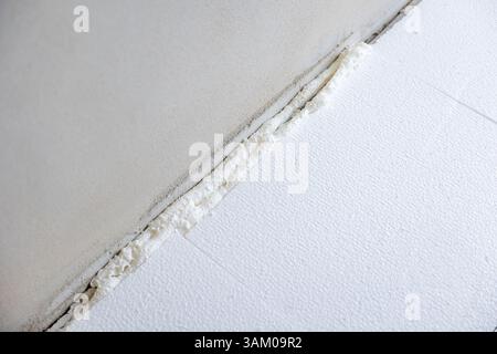 Ouvrier de la construction appliquant une isolation en mousse expansible de polyuréthane sur le sol et le joint mural Banque D'Images