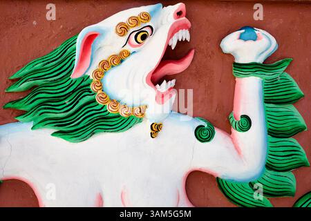 Féroce relief mythique de lion de neige avec crinière flamboyante et bijou, peint sur le mur de plâtre rouge, Ladakh, Inde. Banque D'Images