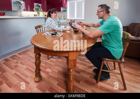 Les adultes plus âgés apprécient le thé à la table ronde en bois dans une atmosphère détendue avec des sièges confortables et des meubles de maison autour d'eux. Banque D'Images