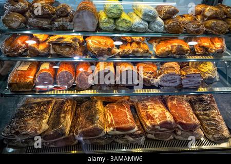 Divers jambons, bacons et charcuteries dans l'emballage sous vide gros plan dans la vitrine en verre de boucherie. Banque D'Images