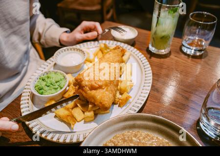 Traditionnel Fish and Chips servi avec une sauce tartare aux pois pâteux sur une assiette dans une table de restaurant Banque D'Images