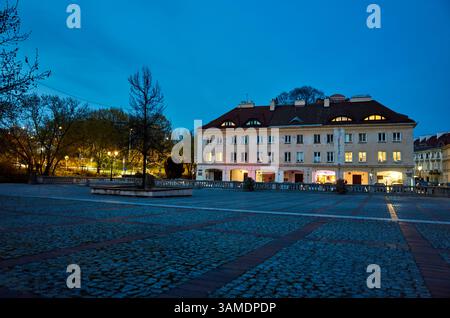Grand bâtiment avec un arbre devant. Le bâtiment est entouré d'une cour avec une fontaine au centre. La cour est vide la nuit, avec seulement quelques lumières éclairant la zone. Vieille ville de Varsovie. Varsovie 13.04.2025 Pologne Banque D'Images