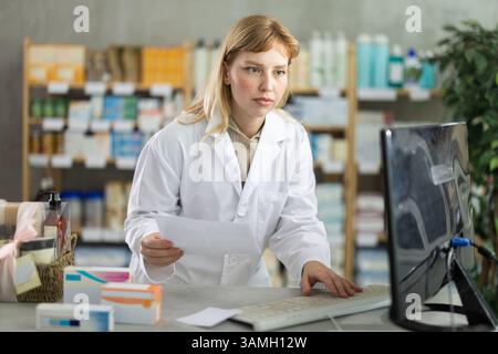 Jeune femme pharmacienne travaillant avec l'ordinateur dans le magasin de pharmacie Banque D'Images