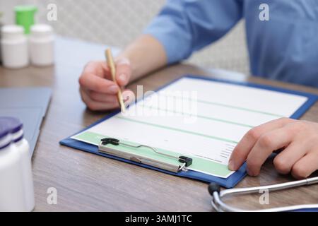 Docteur remplissant la carte médicale du patient à la table en bois, gros plan Banque D'Images
