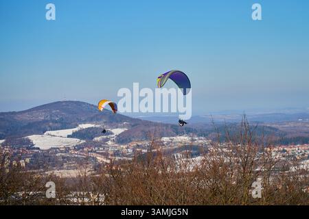 Deux parapentes volent au-dessus du paysage enneigé avec des montagnes et la ville par temps clair. Concept de liberté, d'aventure et de sports de plein air Banque D'Images