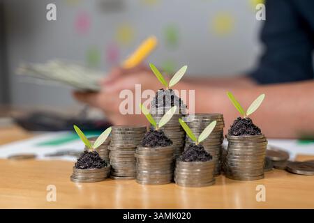 Homme d'affaires écrivant des notes dans le document, modèle de pile de pièces de monnaie dans le fonctionnement des affaires, économiser de l'argent, investir pour la croissance financière à l'avenir. Les semis sont g. Banque D'Images