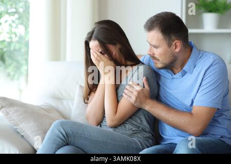 Femme triste réconfortée par un ami ou un partenaire assis sur un canapé à la maison Banque D'Images