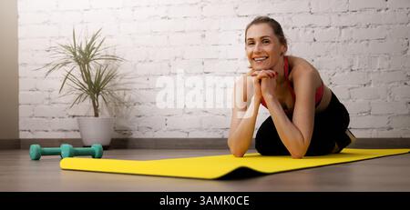 souriant femme instructeur de fitness ou de yoga assis sur un tapis dans la salle de gym. bannière avec espace de copie Banque D'Images