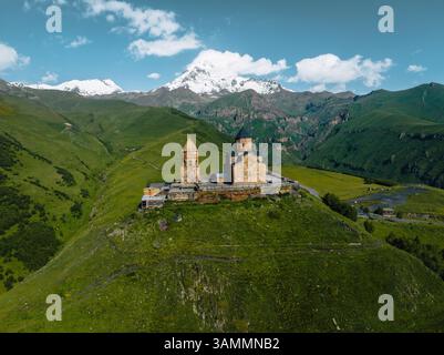 Vue aérienne de l'église gergeti trinity entourée de montagnes majestueuses et d'une vallée tranquille, stepantsminda, géorgie. Banque D'Images