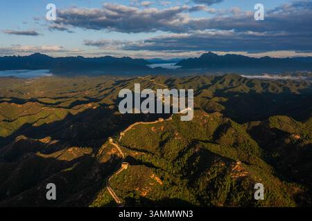 Vue aérienne du grand mur de jinshanling au milieu des montagnes majestueuses et de la vallée sereine au coucher du soleil, chengde, chine. Banque D'Images