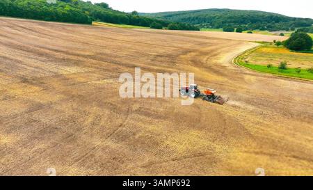 Vue aérienne d'un tracteur travaillant sur une vaste terre agricole. Une vue aérienne panoramique d'un tracteur rouge labourant un grand champ dégagé. Banque D'Images