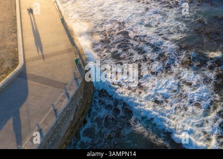 Vue aérienne d'un couple romantique marchant le long de la promenade balnéaire au coucher du soleil, Cape Town, Afrique du Sud. Banque D'Images