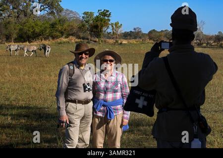 4 mai 2013 - Moremi, Botswana, Afrique - un couple de touristes photographiant avec des zèbres en arrière-plan. Moremi Game Reserve est un parc national du Botswana. Il repose sur le côté est du delta de l'Okavango et a été nommé d'après le chef Moremi de la tribu BaTawana. Moremi a été désignée comme réserve de chasse, et non comme parc national permettant aux BaSarwa ou aux Bushmen de demeurer dans la réserve. (Crédit image : © Sergi Reboredo/ZUMA Wire/ZUMAPRESS.com) Banque D'Images