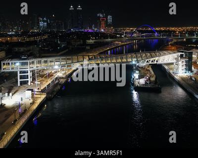 Vue aérienne d'un pont piétonnier torsadé sur le canal de Dubaï illuminé la nuit aux Émirats arabes Unis. Banque D'Images