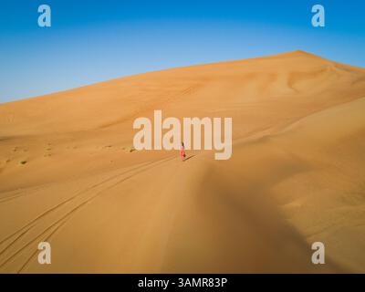 Vue aérienne d'une femme attrayante utilisant une robe rouge dans un paysage désertique, U.A.E. Banque D'Images