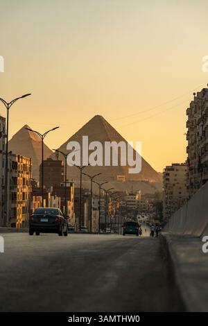 Vue aérienne des pyramides anciennes et du paysage urbain au coucher du soleil avec des bâtiments et des voitures, Gizeh, Egypte. Banque D'Images