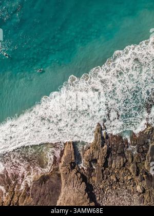 Vue aérienne de la côte avec des vagues qui s'écrasent sur les rochers et un surfeur nageant dans l'eau, Noosa, Queensland, Australie. Banque D'Images