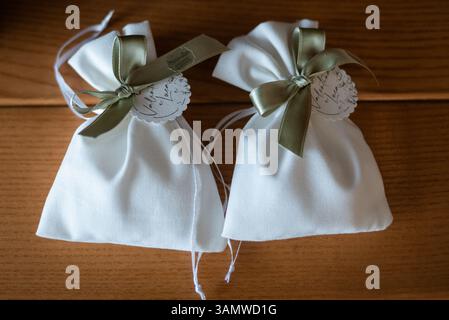 Deux sacs en tissu blanc noués avec des rubans verts reposent sur une surface en bois, présentant une présentation simple mais sophistiquée parfaite pour les cadeaux. Banque D'Images