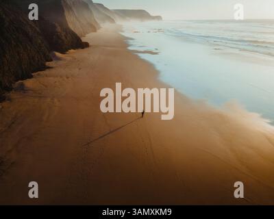 Vue aérienne de la plage sereine de Praia do Cordoama avec personne marchant sur la rive sablonneuse au coucher du soleil, Vila do Bispo, Portugal. Banque D'Images